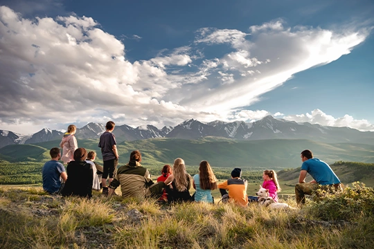 eine Gruppe von Leuten sitzt in der Wiese und schaut auf das Bergpanorama