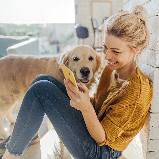 eine Frau schaut aufs Handy, ihr Hund steht daneben