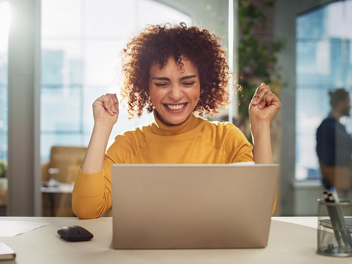 Eine junge Frau sitzt vor dem Laptop und freut sich