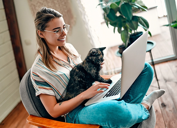 Eine junge Frau sitzt mit dem Laptop und einer Katze auf einem Sessel