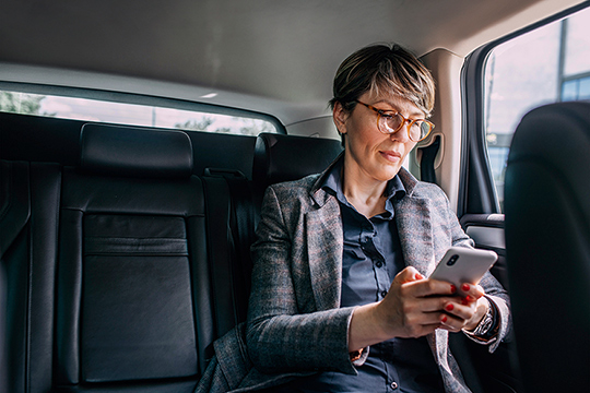 Eine Frau sitz auf der Rückbank eines Autos und schaut auf ihr Handy