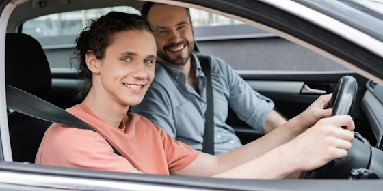 Ein junger Mann sitzt am Steuer eines Autos, sein Vater daneben