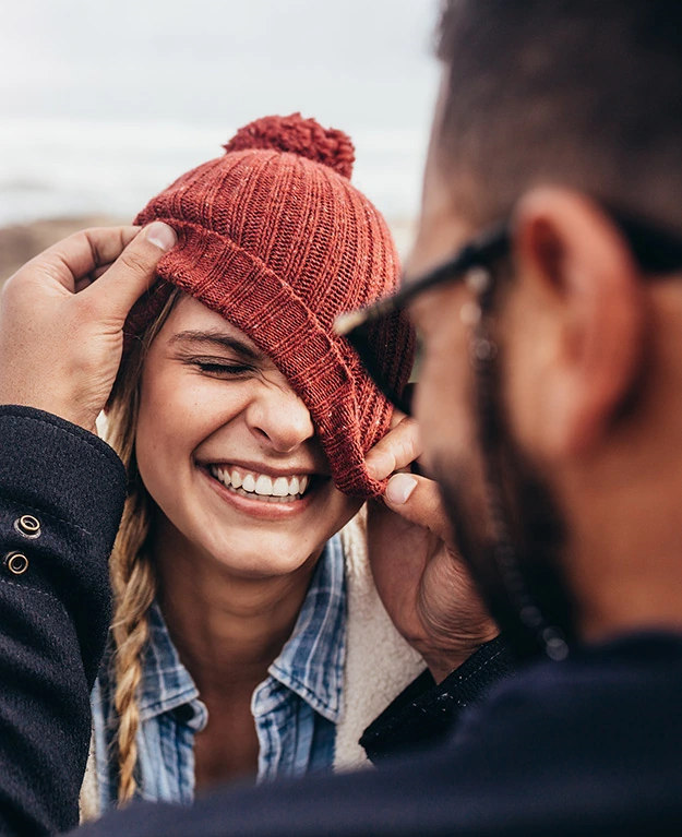 Eine junge Frau mit Haube lacht einen jungen Mann an