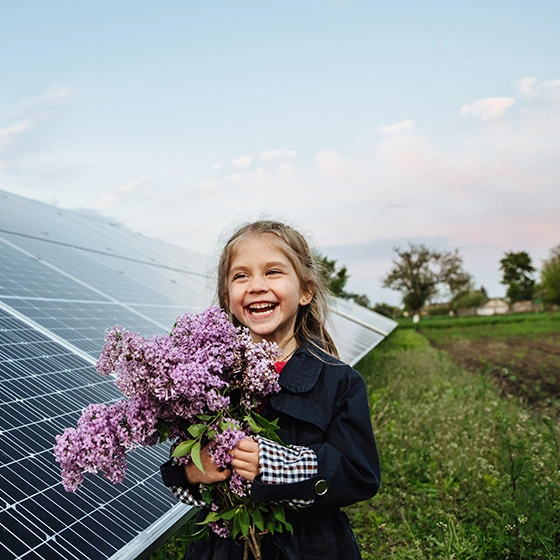 Ein Mädchen steht vor einer Photovoltaikanlage und hält Blumen in der Hand