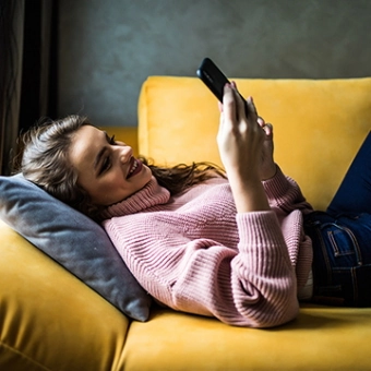 Frau liegt mit Smartphone auf dem Sofa