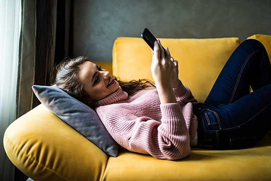 eine Frau lieg tmit dem Handy auf der Couch