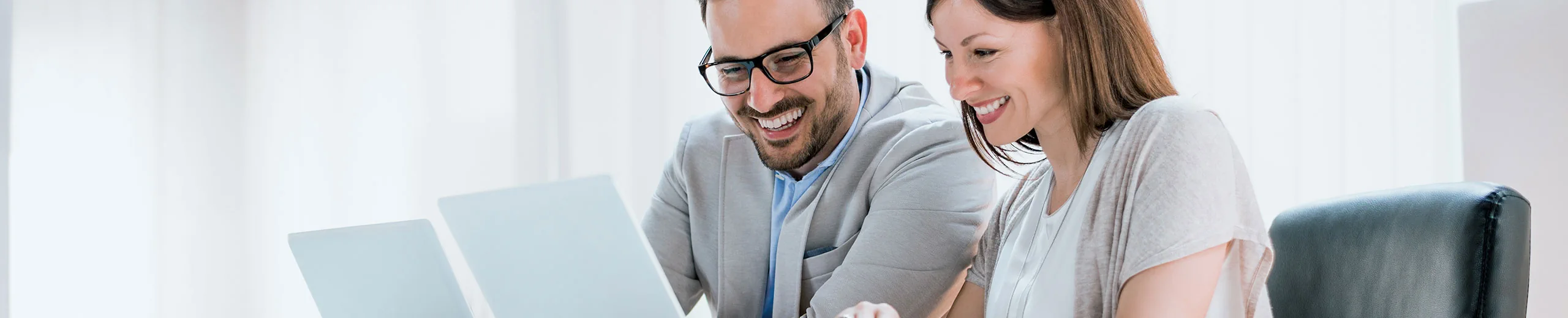 Zwei Personen sitzen nebeneinander, unterhalten sich und arbeiten auf dem Laptop