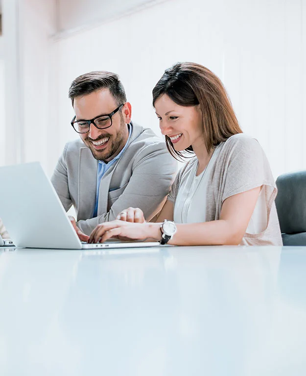 Zwei Personen sitzen nebeneinander, unterhalten sich und arbeiten auf dem Laptop