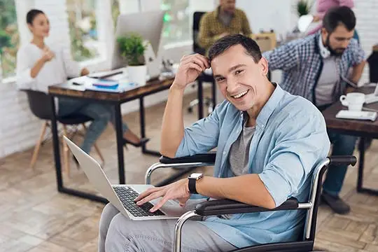 Mann mit einem Laptop auf dem Schoß sitzt in einem Rollstuhl