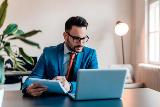 A man in a blue suit is sitting in front of his laptop