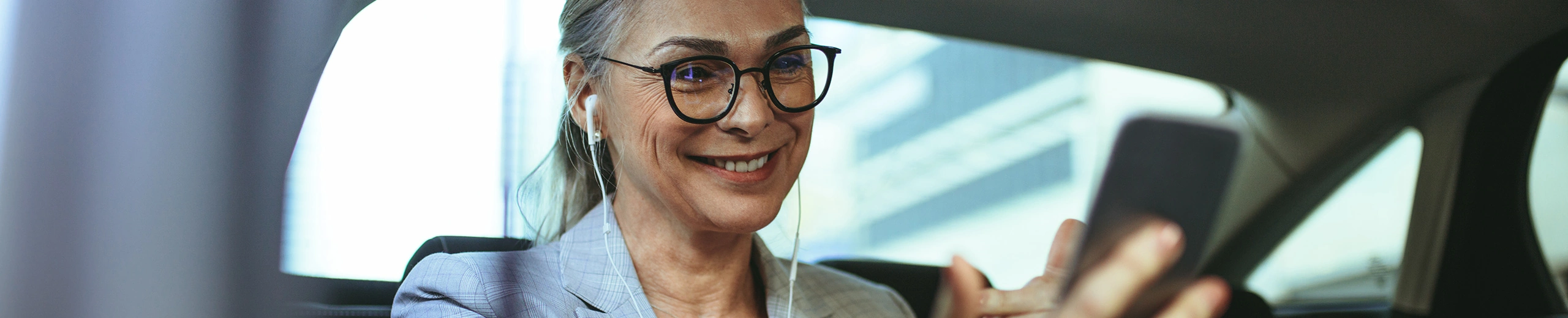 Eine Frau sitzt mit ihrem Handy in der Hand auf der Rücksitzbank eines Autos