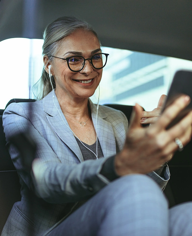 Eine Frau sitzt mit ihrem Handy in der Hand auf der Rücksitzbank eines Autos