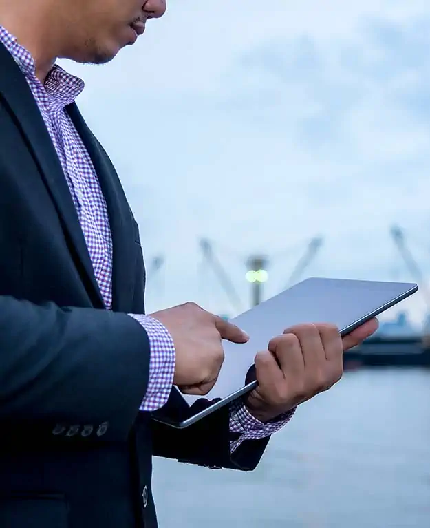 Ein Mann tippt auf seinem Tablet, im Hintergrund ist ein Hafen zu sehen