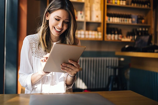 Eine junge Frau schaut lachend auf ihr Tablet