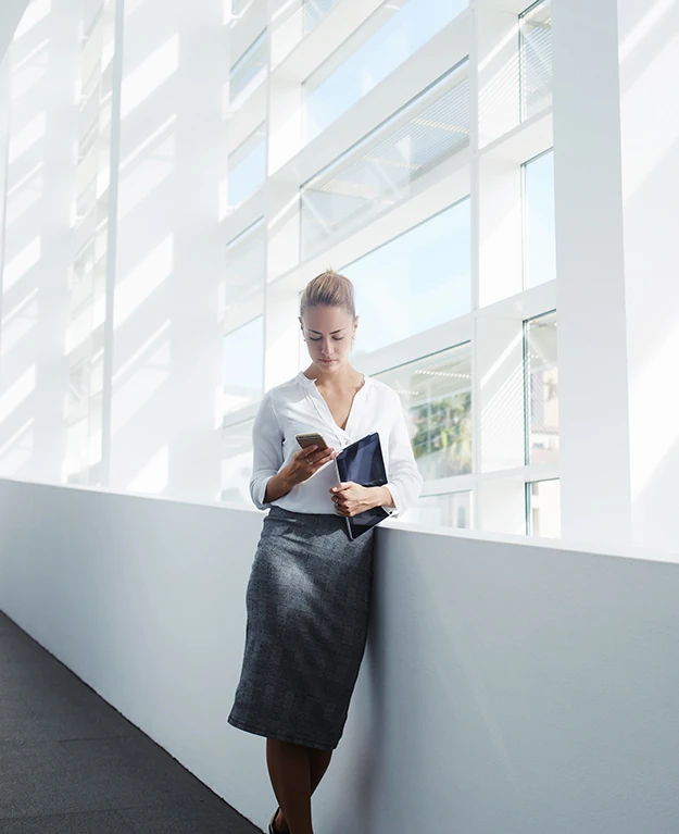 Eine Businessfrau steht mit ihrem Handy an eine Wand angelehnt