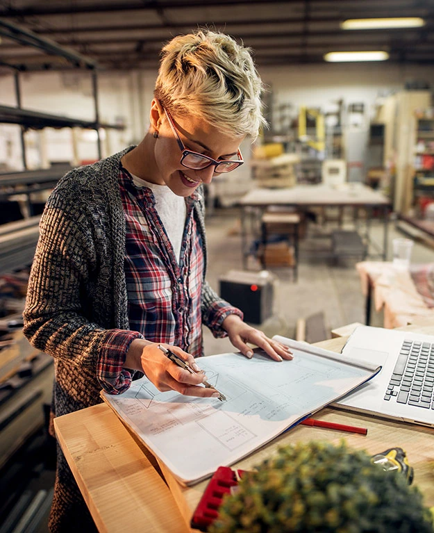 Eine Frau steht in einer Werkstatt vor dem Laptop