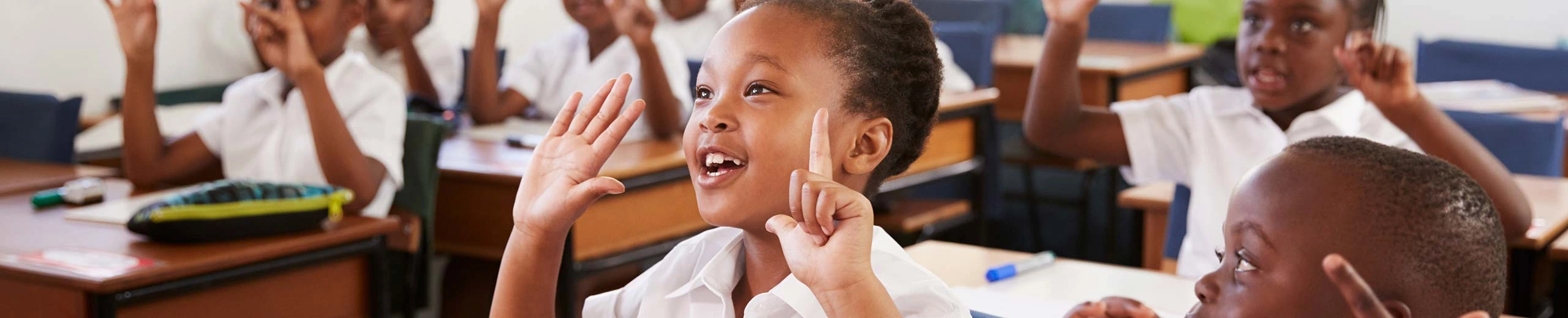 Kleines Kind sitzt in einer Schulklasse und deutet mit den Händen die Zahl Sieben