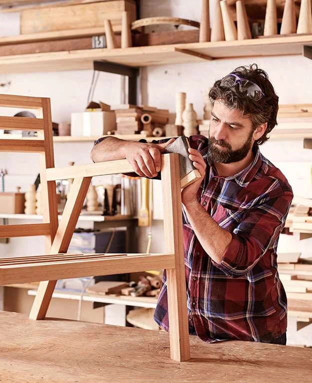 Mann schleift eine Holzbank in einer Tischlerei