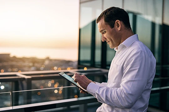 Ein Mann steht am Balkon und liest am Tablet