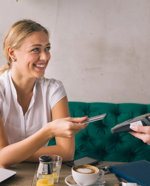 Eine Frau im Cafe bezahlt mit ihrer Debitkarte auf einer POS Kasse