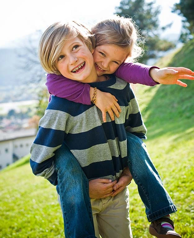 Mädchen sitzt auf dem Rücken eines Jungen, beide lachen