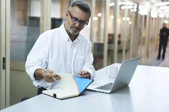 Mann blickt auf Aktenstoß und arbeitet am Computer.