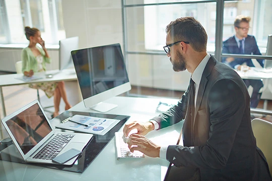 Ein Mann sitzt vor einem Computer, im Hintergrund sieht man andere Personen