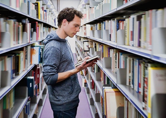 Ein junger Mann steht zwichen den Bücherregalen in einer Bibliothek