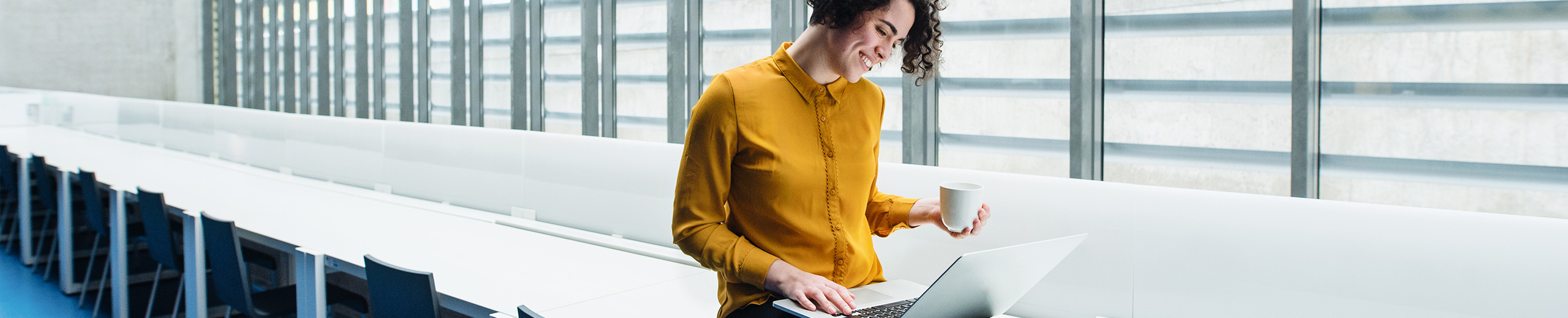 Woman with yellow blouse looks into her laptop