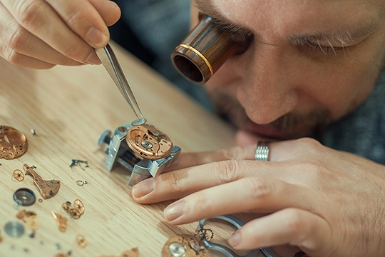 Ein Uhrmacher arbeitet mit einer Lupe und einer Pinzette an einer Uhr