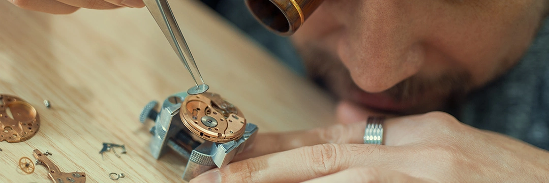 A watchmaker works with a magnifying glass and tweezers on a watch.