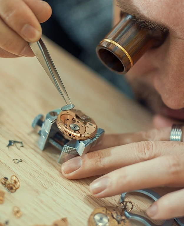 Ein Uhrmacher arbeitet mit einer Lupe und einer Pinzette an einer Uhr