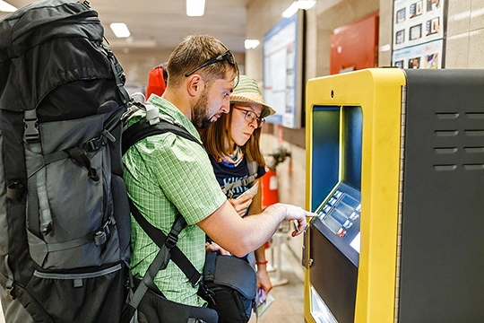 Ein Mann mit einem großen Rucksack und eine Frau mit Strohhut stehen vor einem Automaten