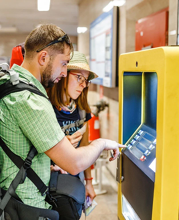 Ein Mann mit einem großen Rucksack steht vor einem Automaten mit der Bankomatkarte in der Hand