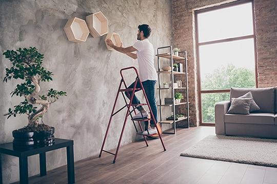 Mann steht auf Leiter und montiert Regale an der Wand.