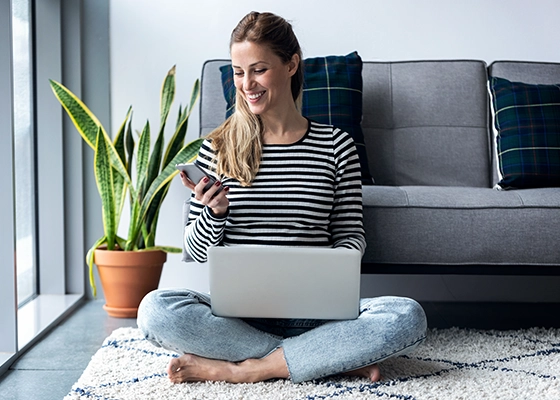 eine Frau sitz am Boden mit ihrem Laptop und Handy