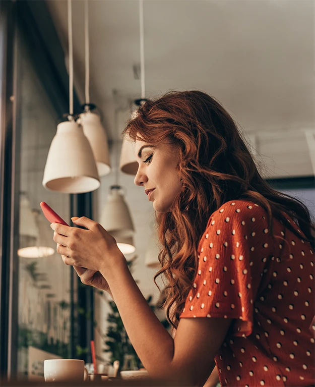 Frau mit rötlichen Haaren ist seitlich zu sehen, wie sie auf ihr Handy schaut