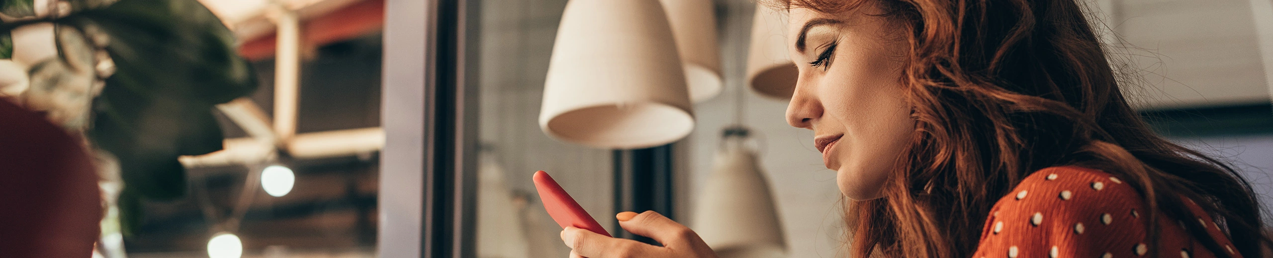 Frau mit rötlichen Haaren ist seitlich zu sehen, wie sie auf ihr Handy schaut