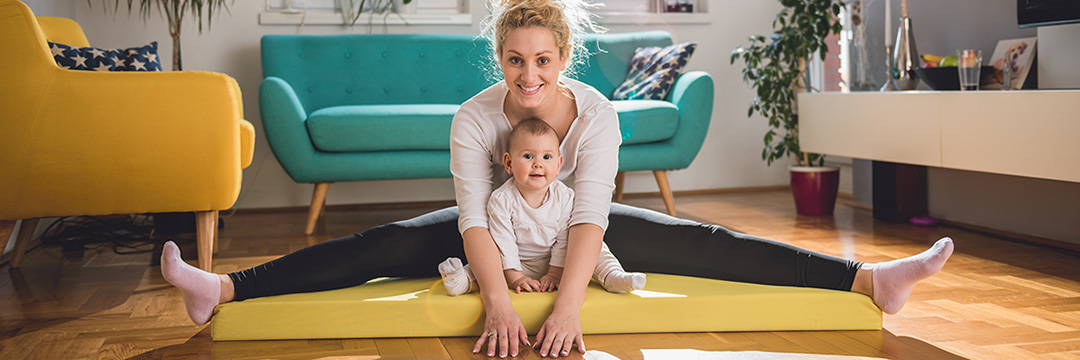 Eine Mutter sitzt mit ihrem Kind auf einer Yogamatte 