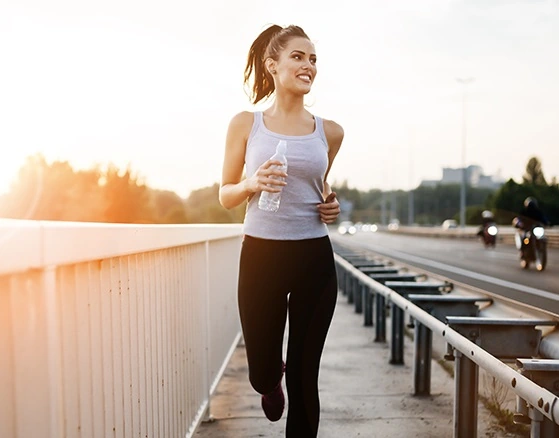 Eine junge Frau joggt mit einer Wasserflasche in der Hand