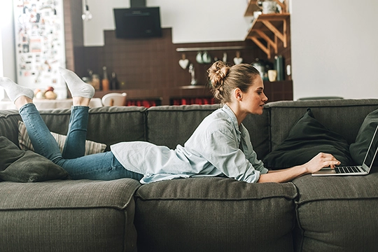 Eine Studentin liegt mit ihrem Laptop auf der Couch