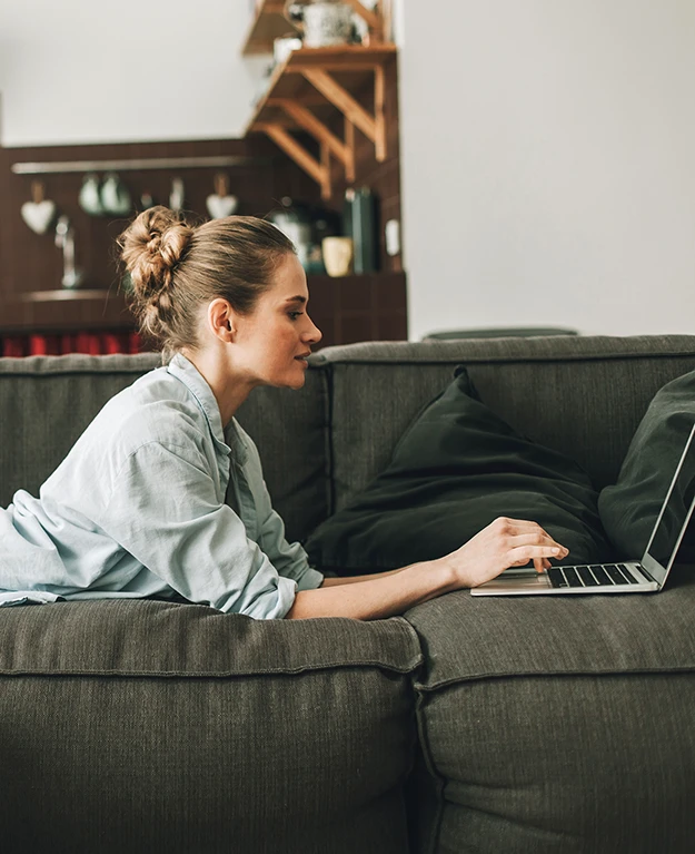 eine junge Frau liegt auf der Couch vor dem Laptop