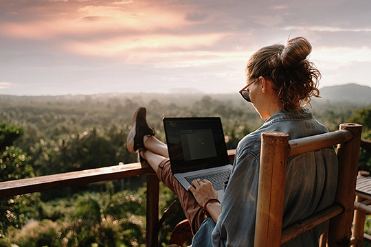 Eine Frau schaut auf einem Balkon  auf ihren Laptop