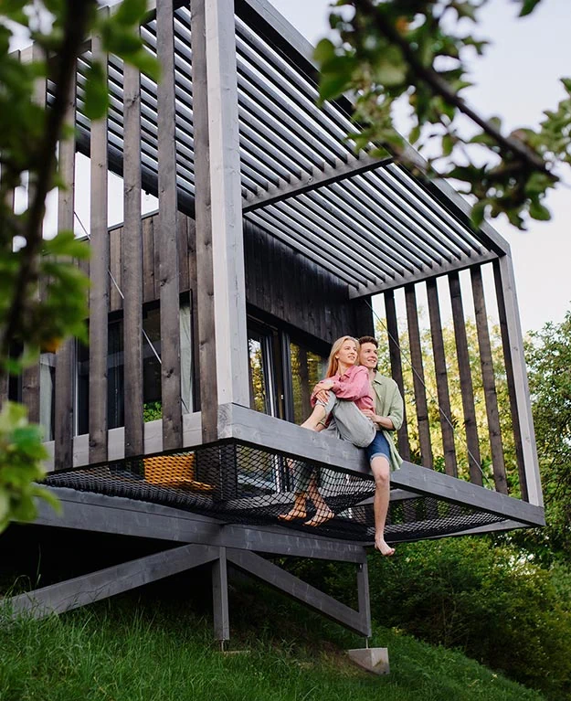 Ein junges Paar sitztauf der Terrasse ihres Holzhauses im Grünen