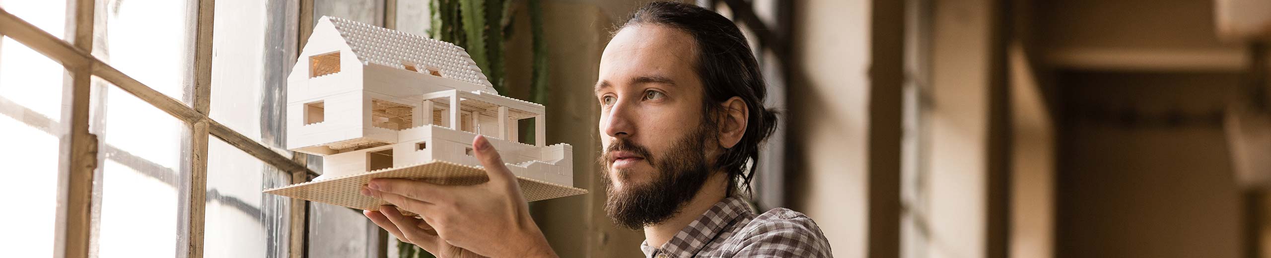 Mann hält ein Modellhaus in der Hand und blickt aus dem Fenster