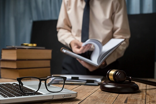 Tisch mit Laptop, Brille und Richterhammer. Mann mit Buch im hintergrund