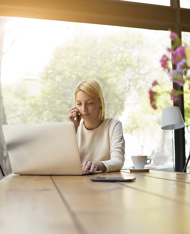 Junge Frau arbeitet am Laptop, vor ihr steht ein Strauß Blumen