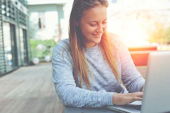 Junge Frau sitzt am Computer und lächelt.