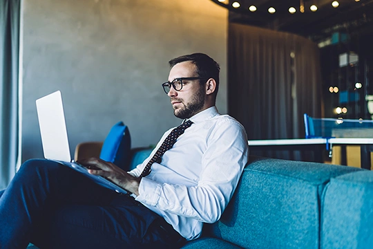 Mann im Anzug sitzt auf Couch und arbeitet am Laptop