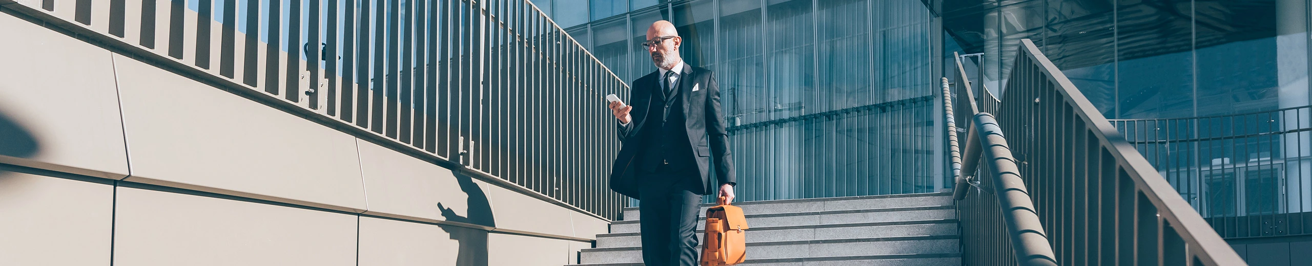 Ein Mann im Anzug mit Aktentasche und Handy geht über eine Stiege vor einem Bürogebäude